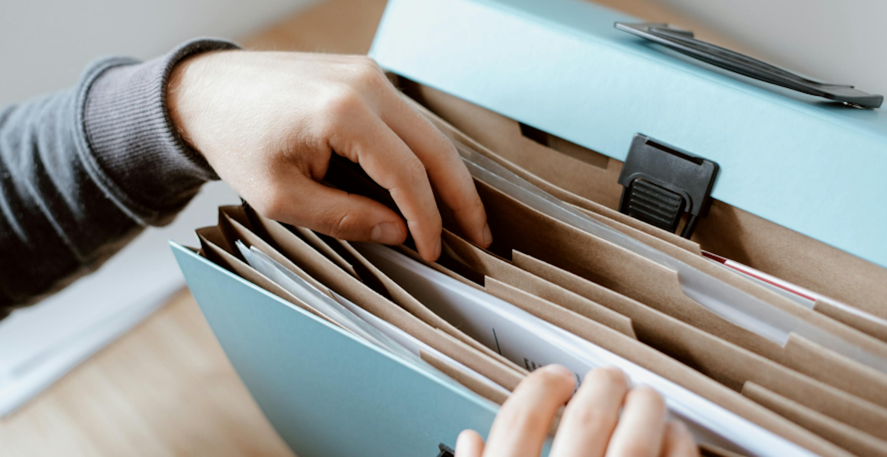 hands searching through files in a light blue file cabinet