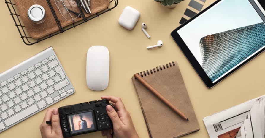 persons desk with airbods, phone, notebook, and tablet