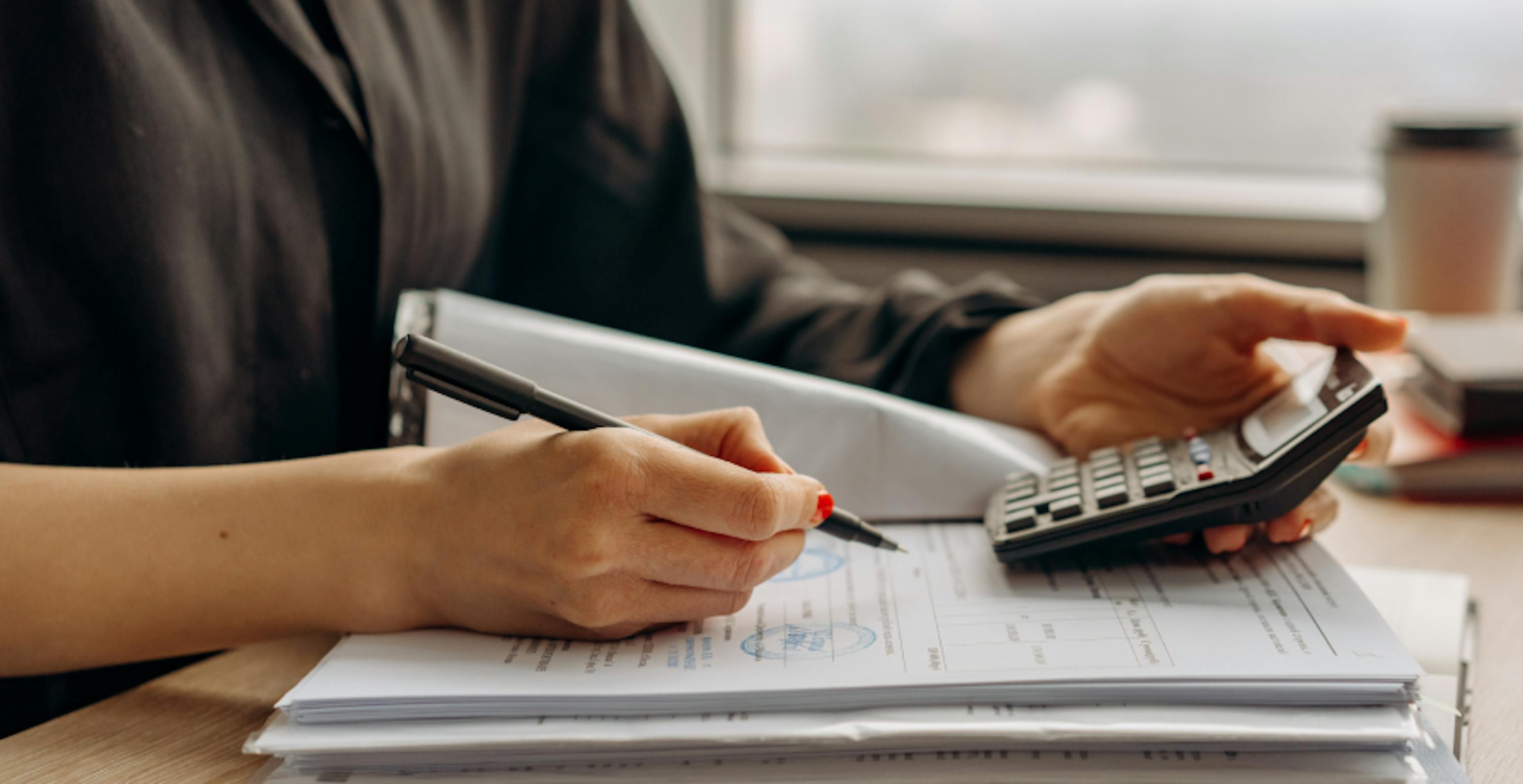 une femme tenant une calculatrice dans une main et un stylo dans l'autre pour écrire sur un document papier