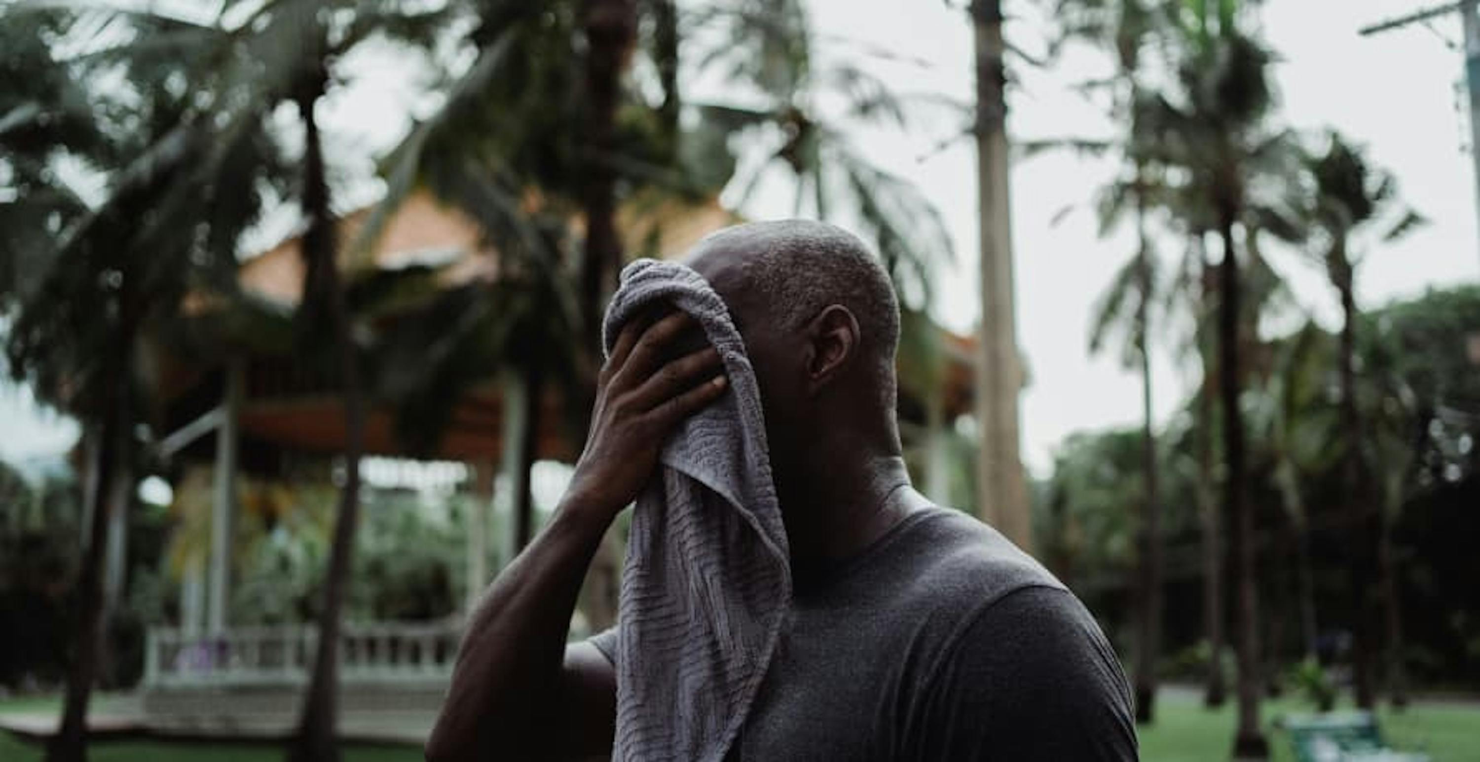 man in a city garden wiping sweat from his face