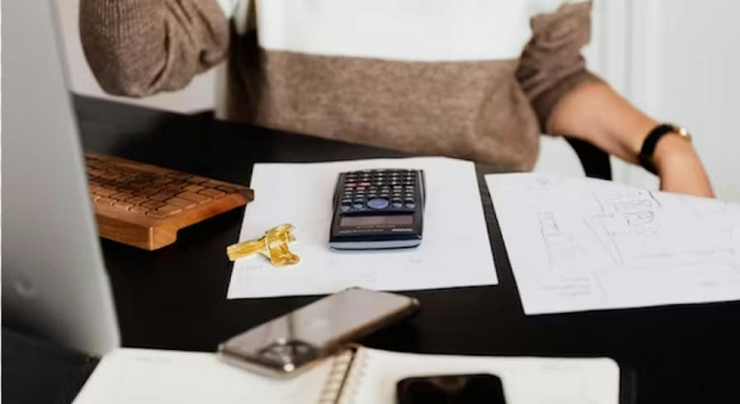 Woman sitting at table with calculator, document and smartphone