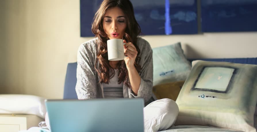 person in bed with coffee on computer