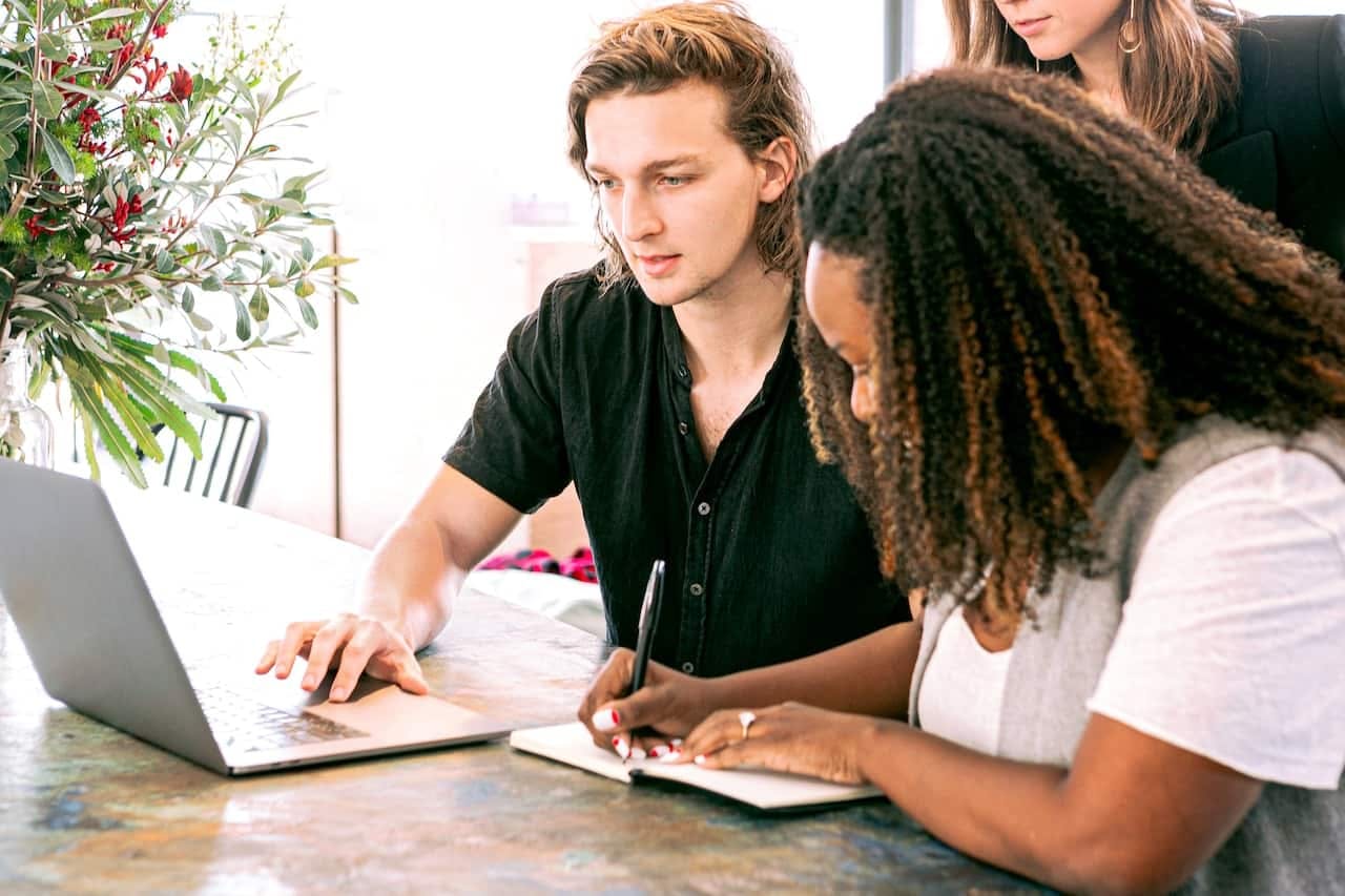 Homme travaillant sur son ordinateur portable pendant qu'une femme prend des notes