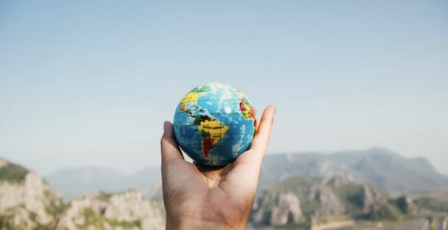 a hand holding a globe with mountains view