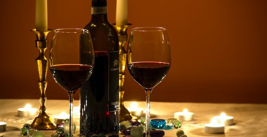 dark wine bottle with two glasses one third full and small, flat candles on table