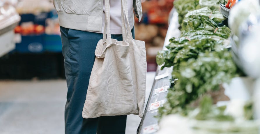 une personne avec un tote bag devant le rayon salades d'un supermarché