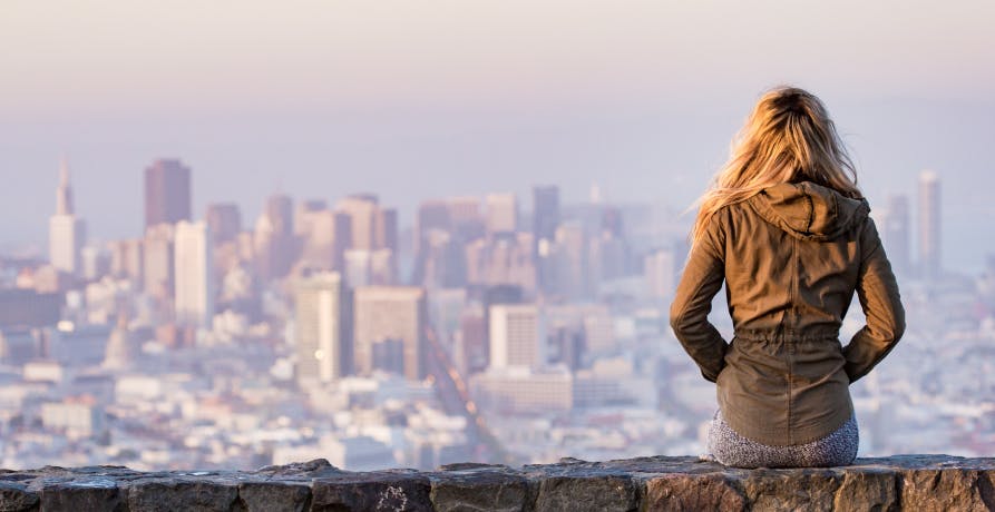femme assise de dos sur un muret avec un aperçu de la ville