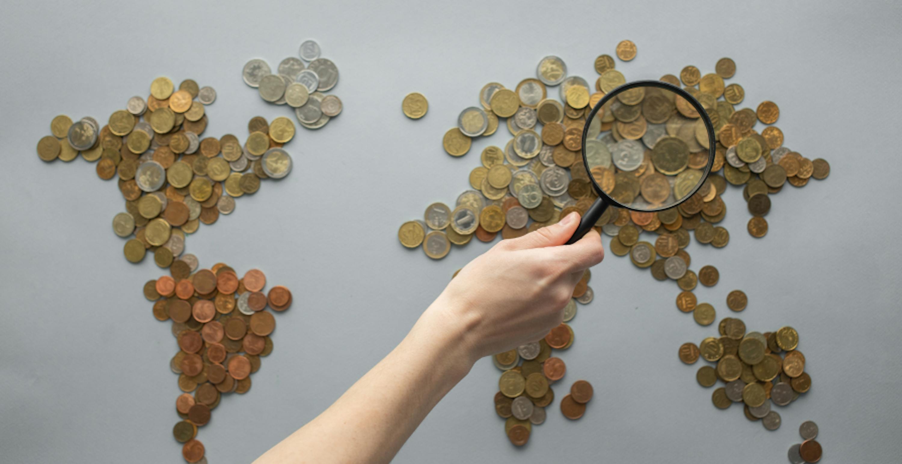 person holding magnifying glass over coins in shape of a map of the world