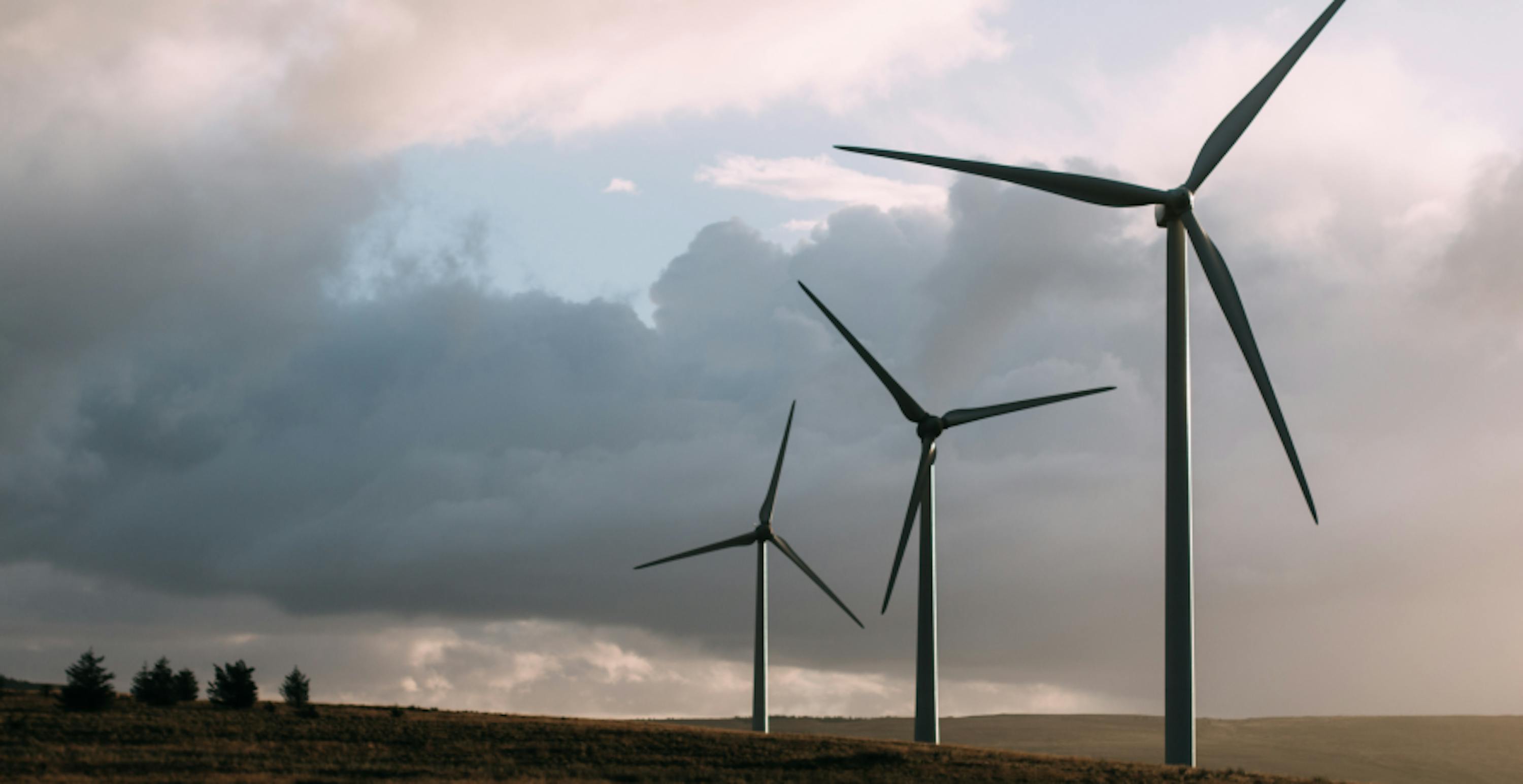 wind turbines against clouds and small trees in bottom left hand side 