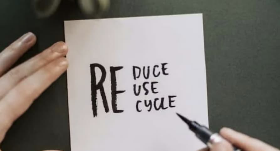 Person holding pen above paper "reduce, reuse, recycle"