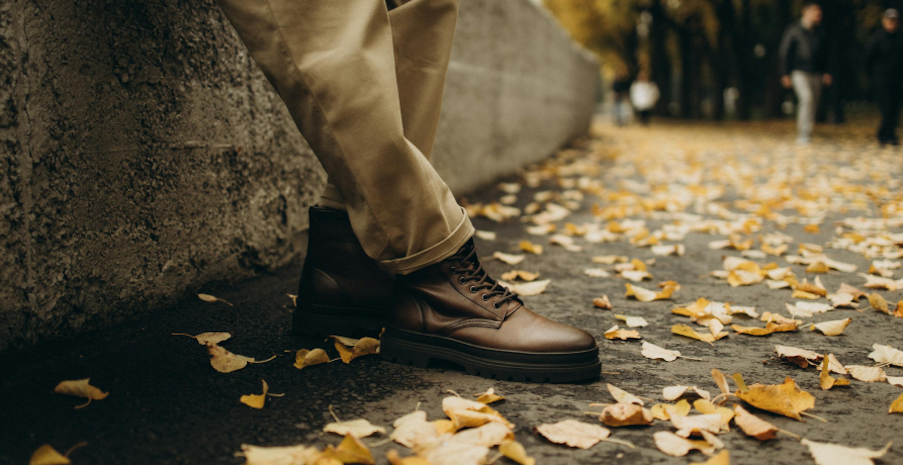 une personne debout sur le trottoir devant des feuilles mortes sur le sol