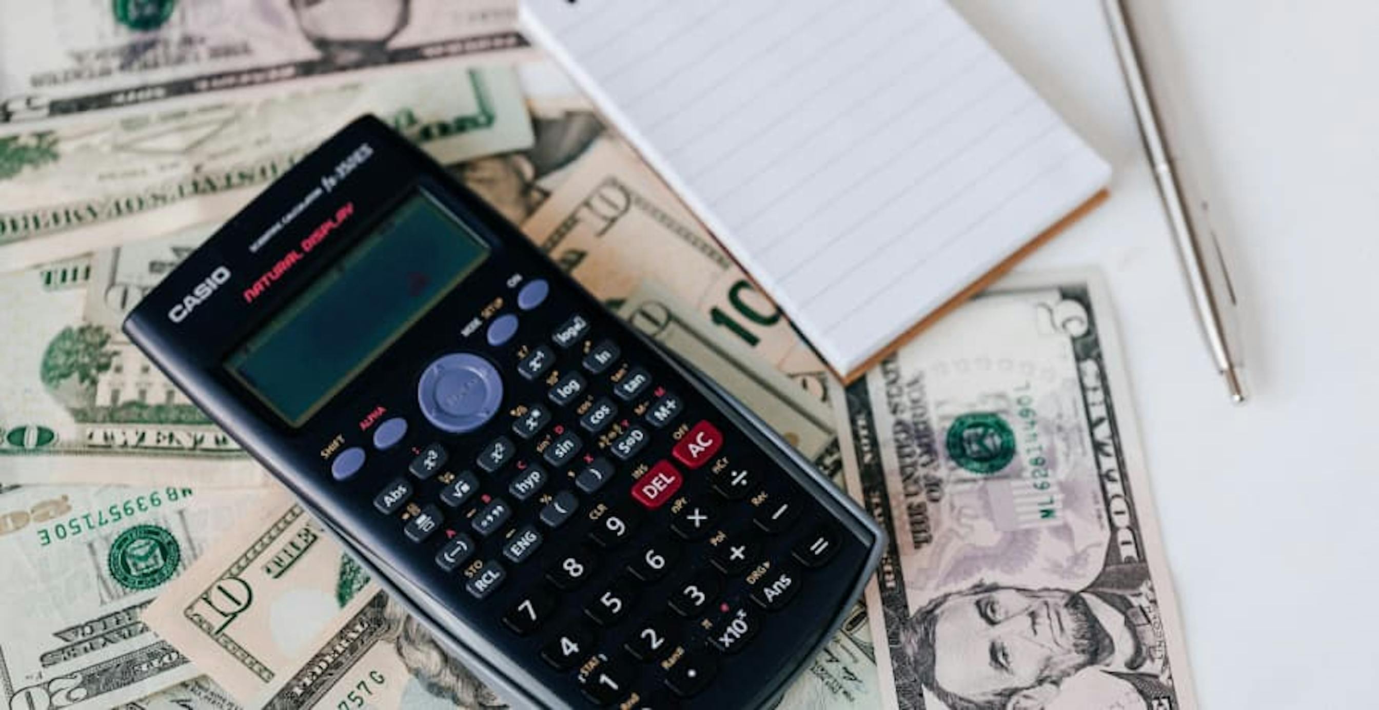 calculator and notepad on top of usd bills