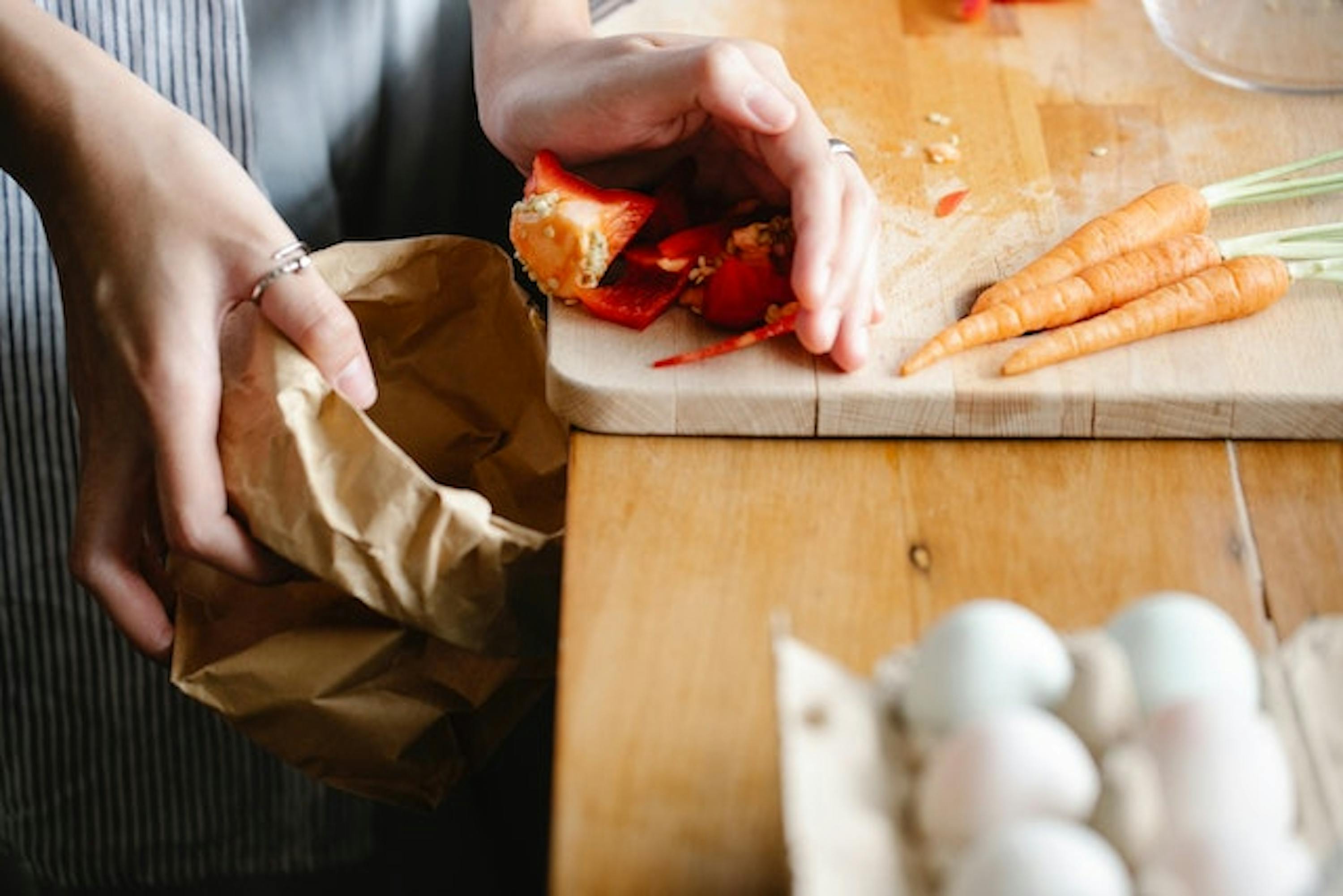 Une personne qui met les restes de légumes dans un sac en carton