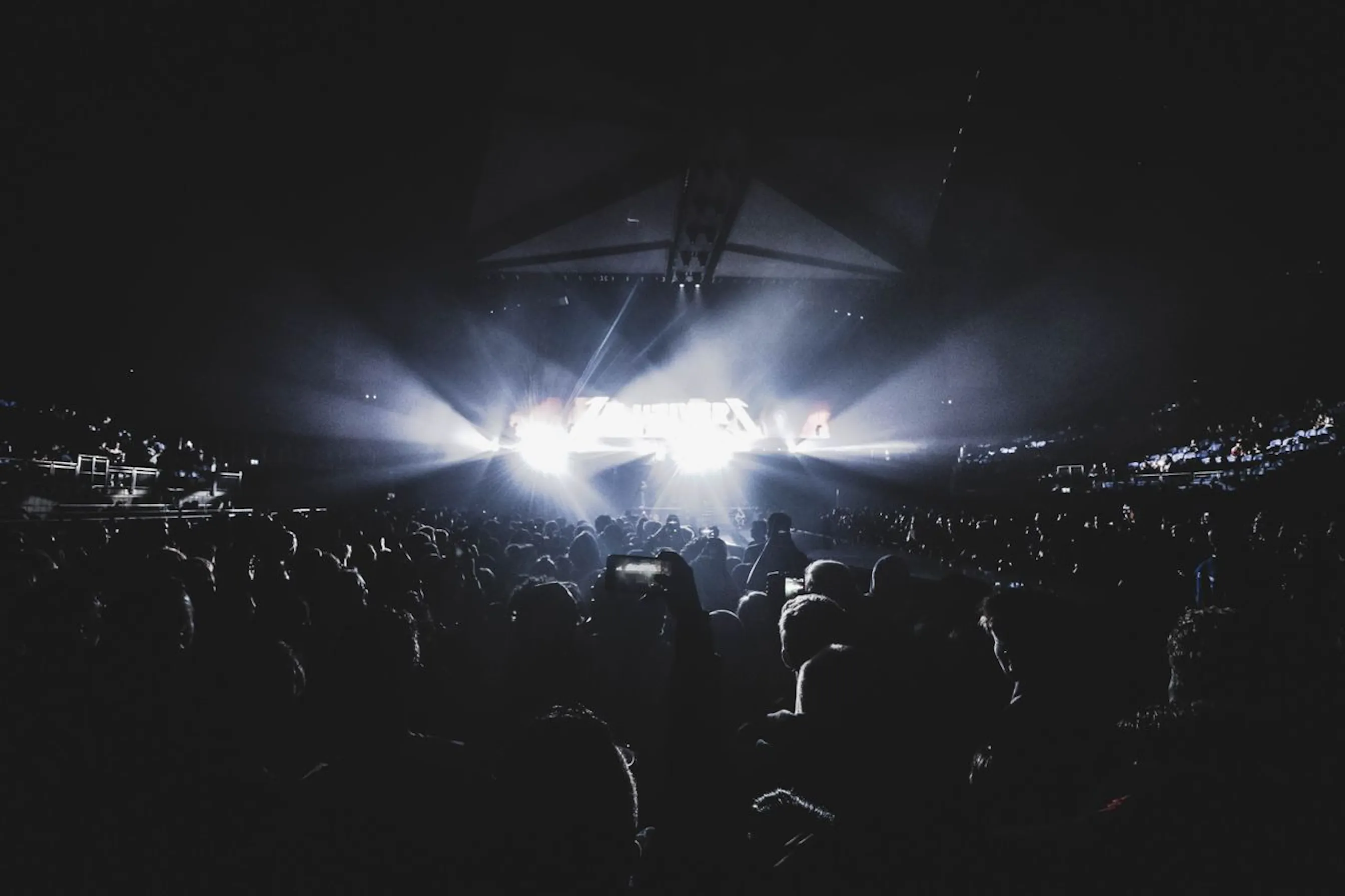 Silhouettes de spectateurs face à une scène de concert illuminée, de nuit.