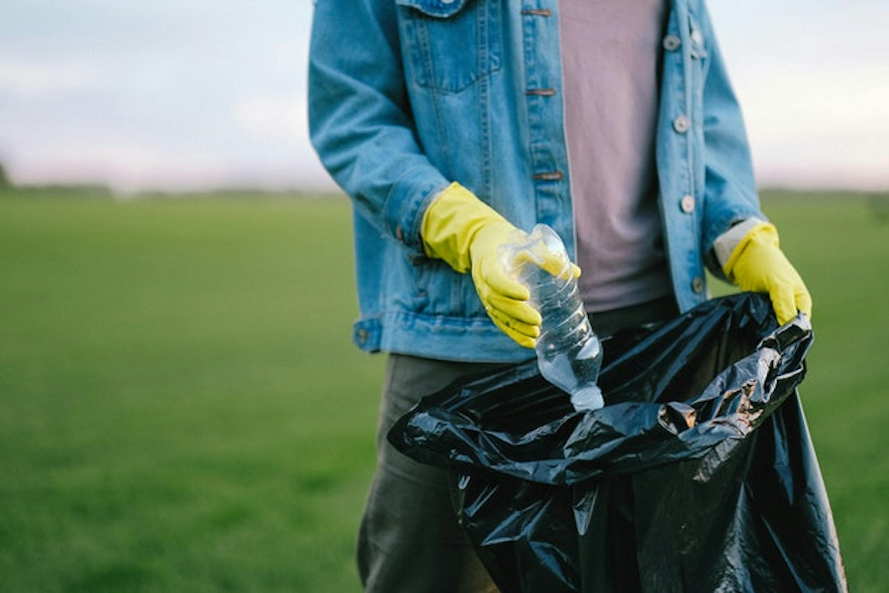 Personne qui met une bouteille en plastique dans un sac poubelle noir