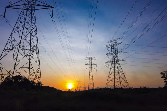Pylônes électriques à haute tension en silhouette contre un ciel de coucher de soleil.