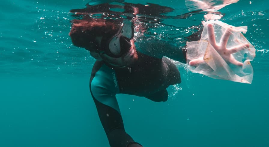 person underwater reaching for a plastic bag