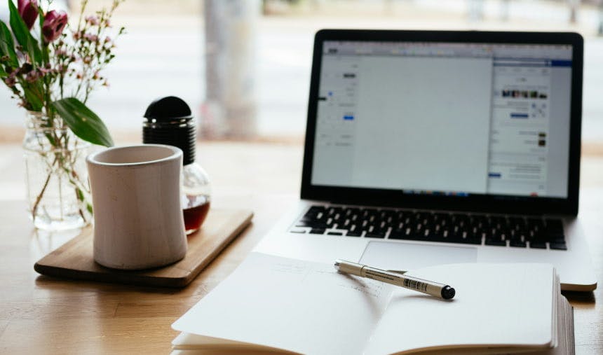 laptop next to plant coffee and notebook