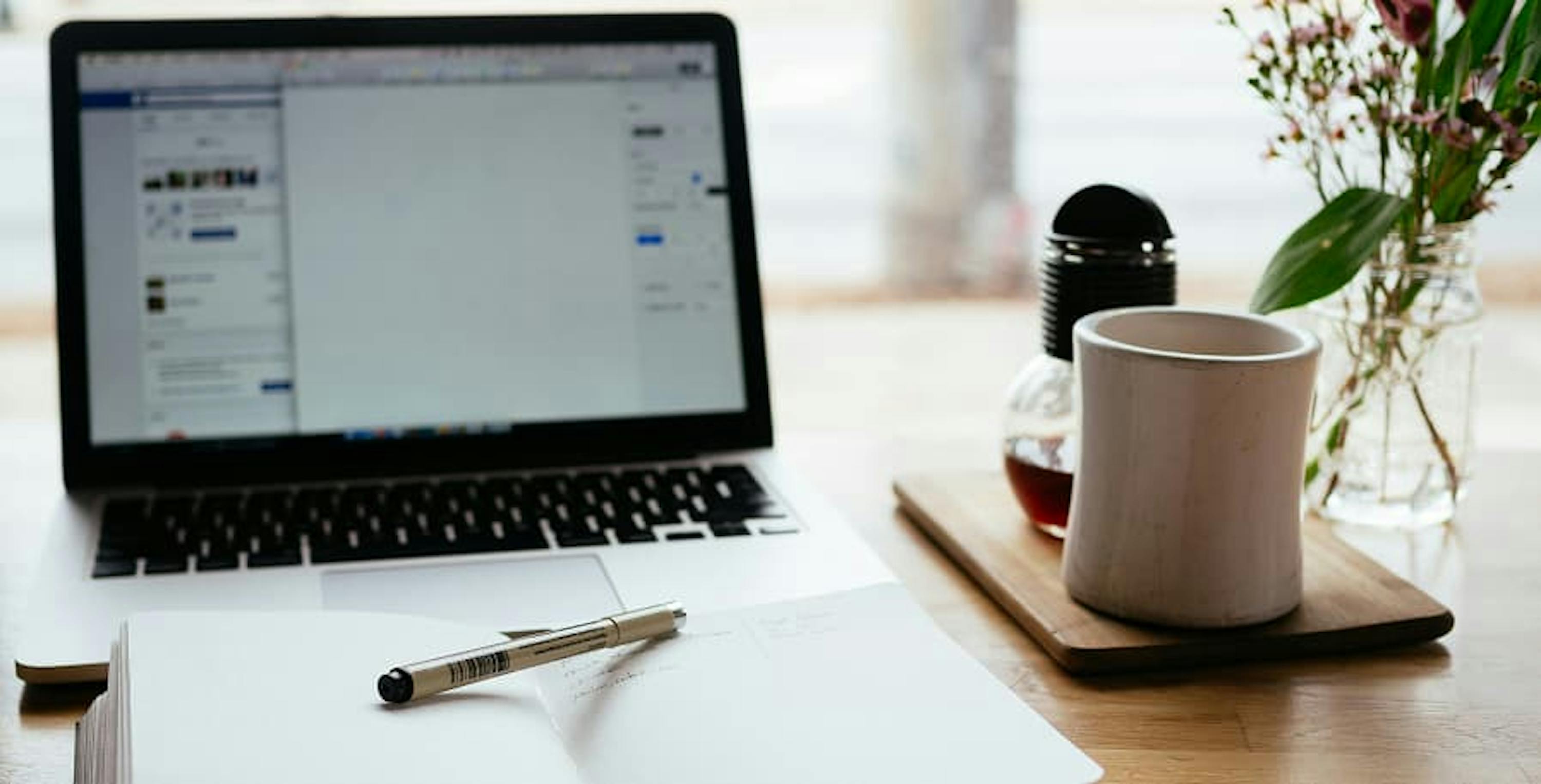 laptop next to coffee and notebook with pen