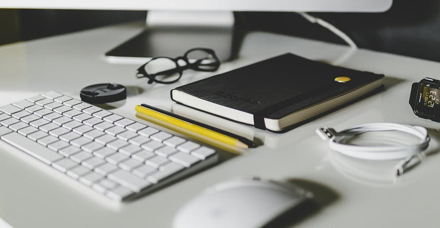 glasses, keyboard, mouse, and black notebook on white desk