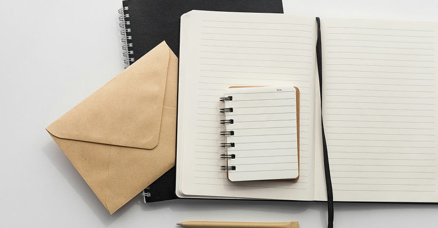 brown envelope, open note book and mini one on top of it all resting on one large black notebook