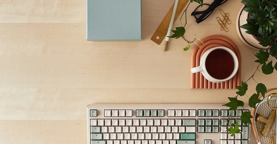 keyboard on wooden table with coffee and plant