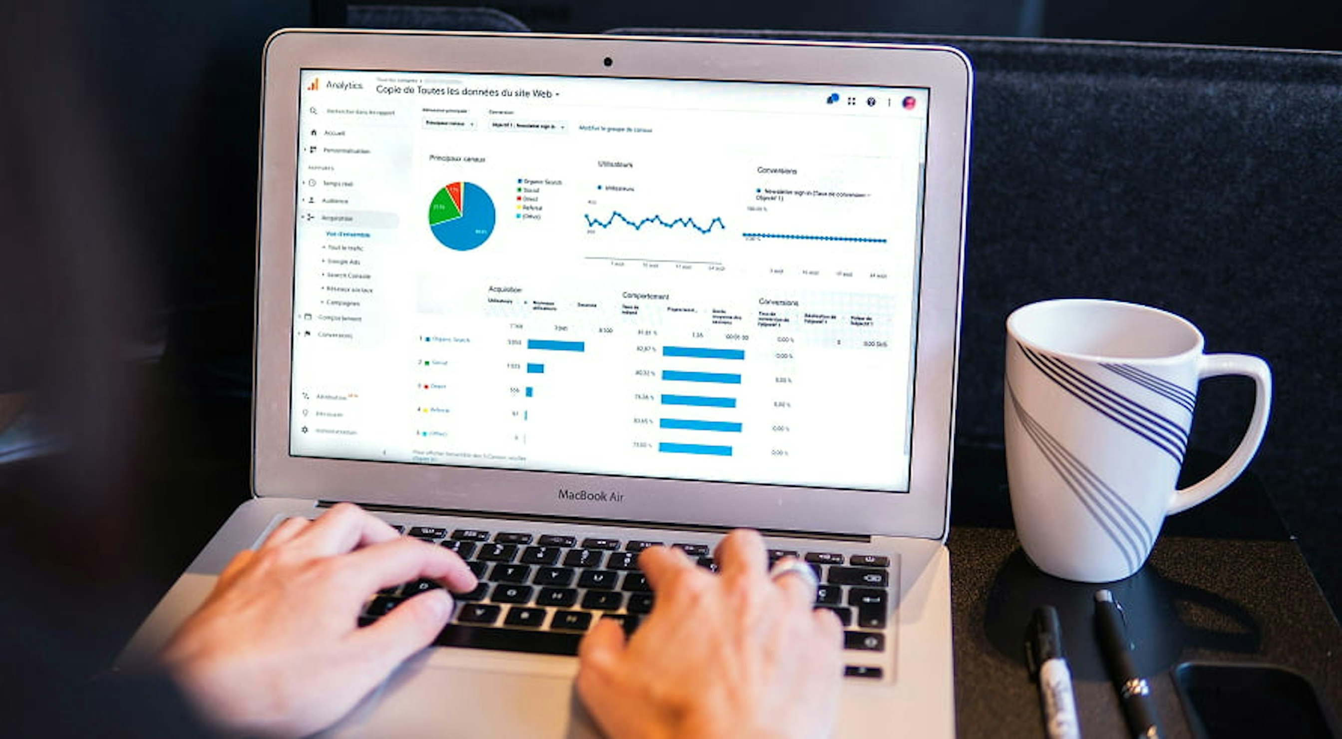 person looking at graphs on small macbook air with coffee