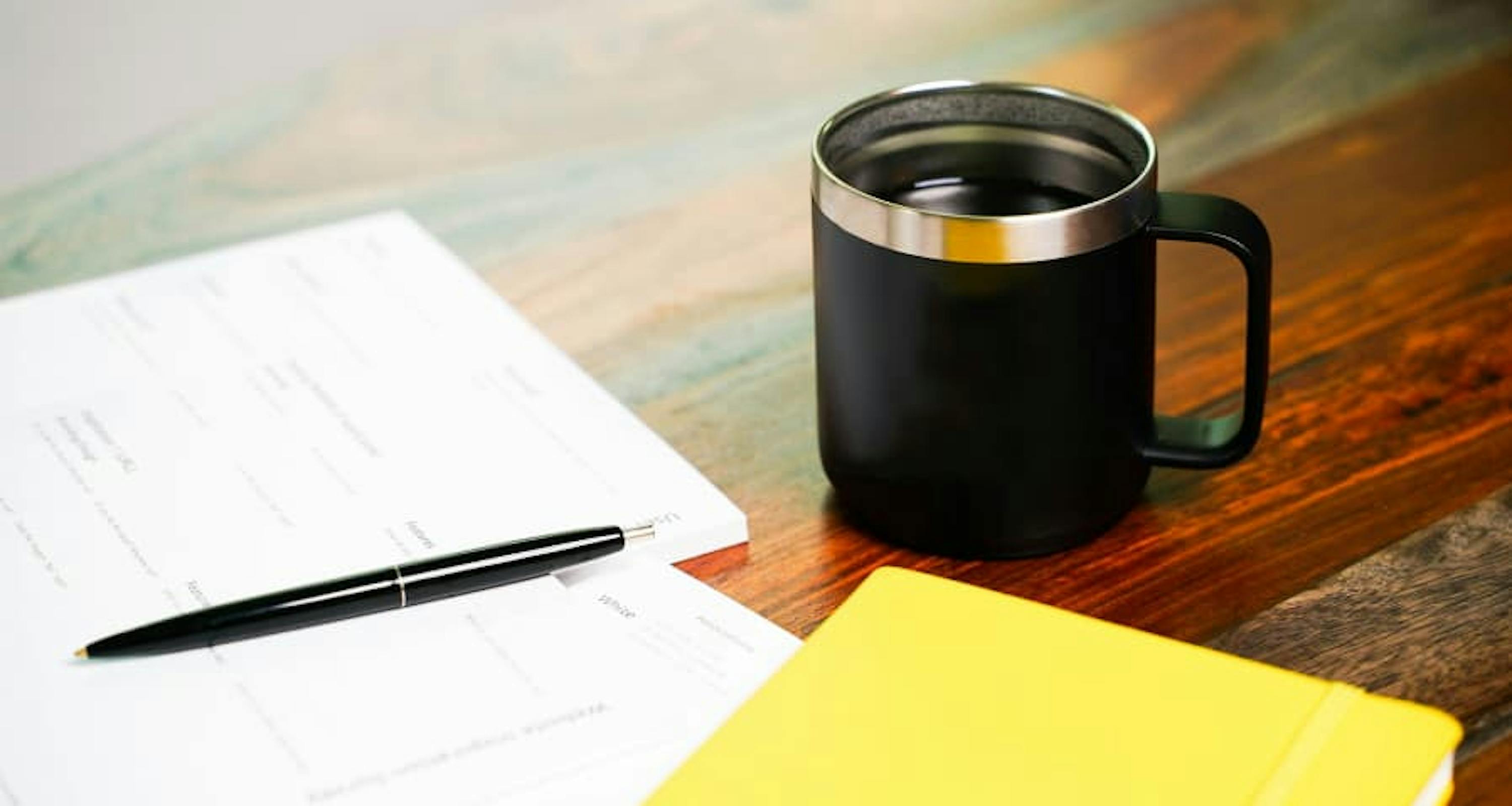 pen, paper, yellow notebook, and coffee mug