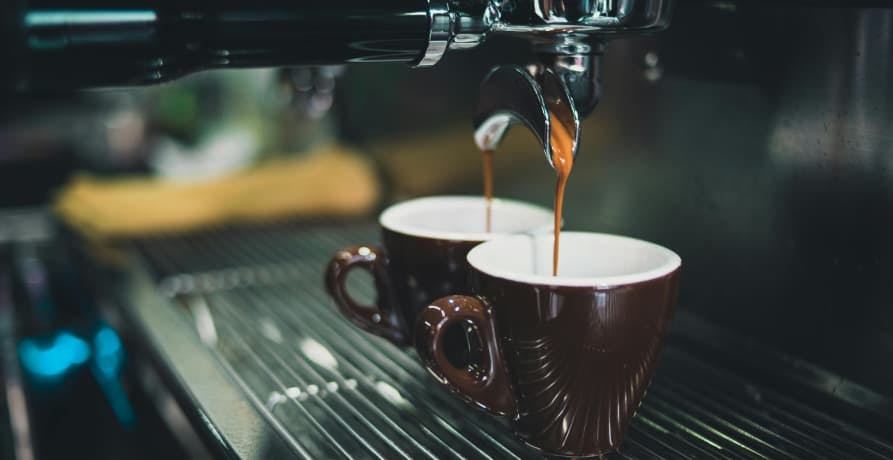 two cups of coffee being prepared by a coffee machine