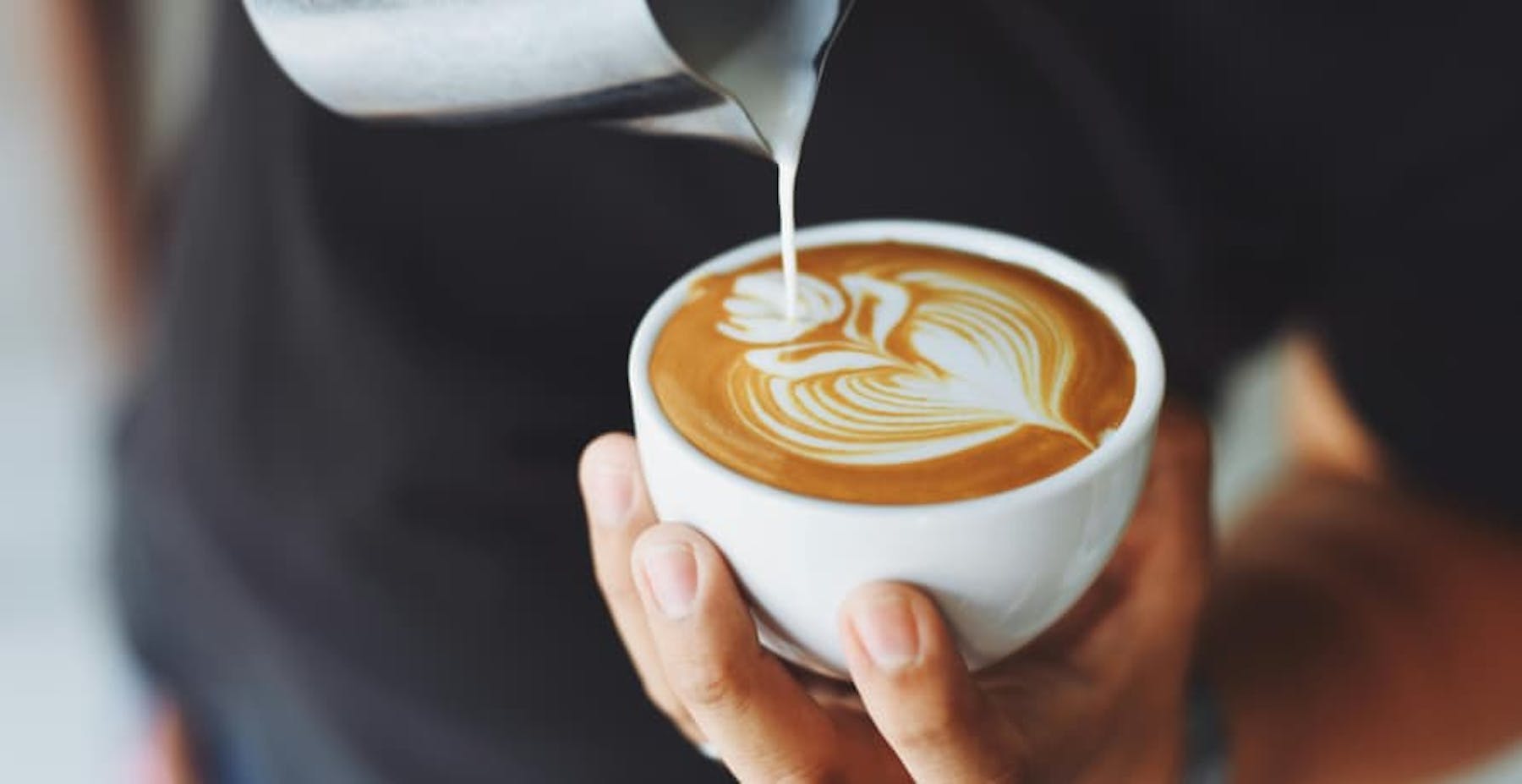 Someone pouring milk into a coup of coffee