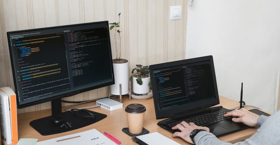 person coding on a laptop with desktop beside it