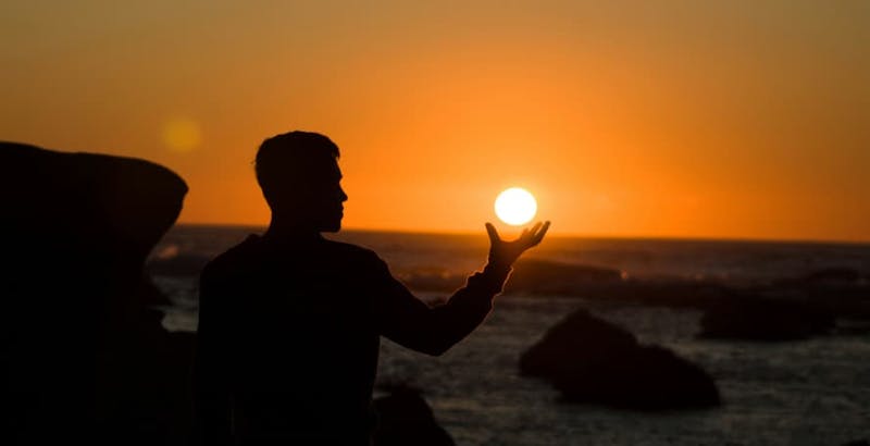 person pretending to be holding the sun at sunset