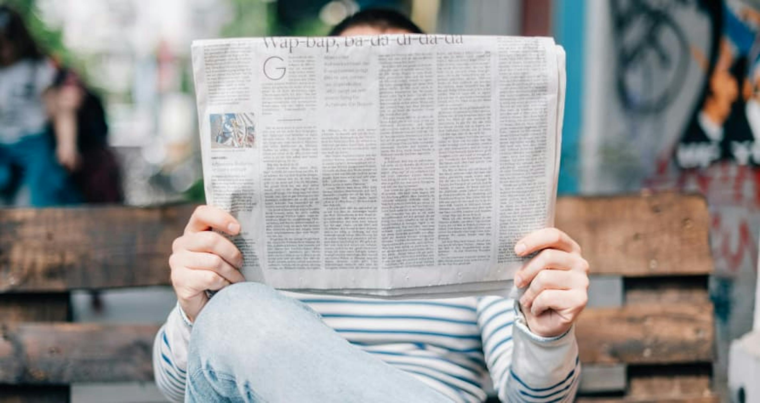 person reading newspaper on bench