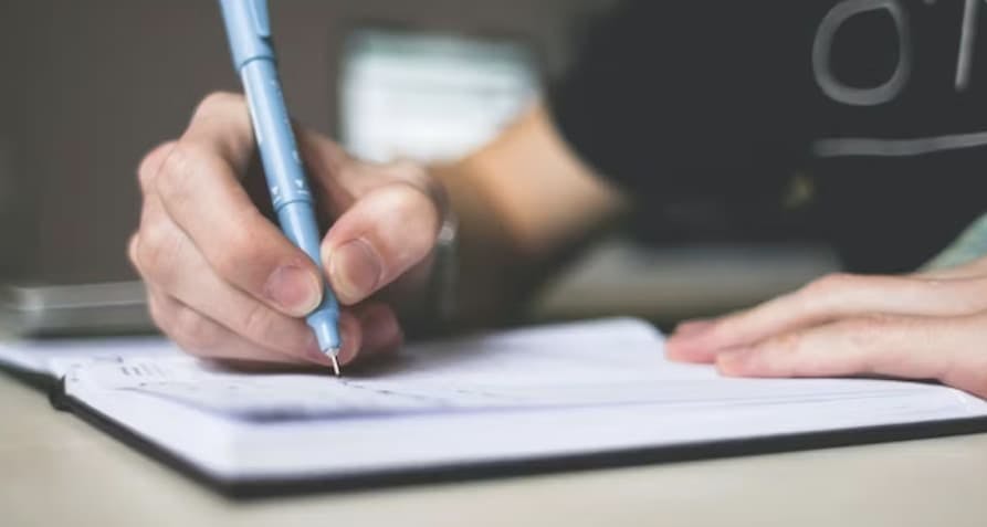 Person holding blue ballpoint pen writing in book