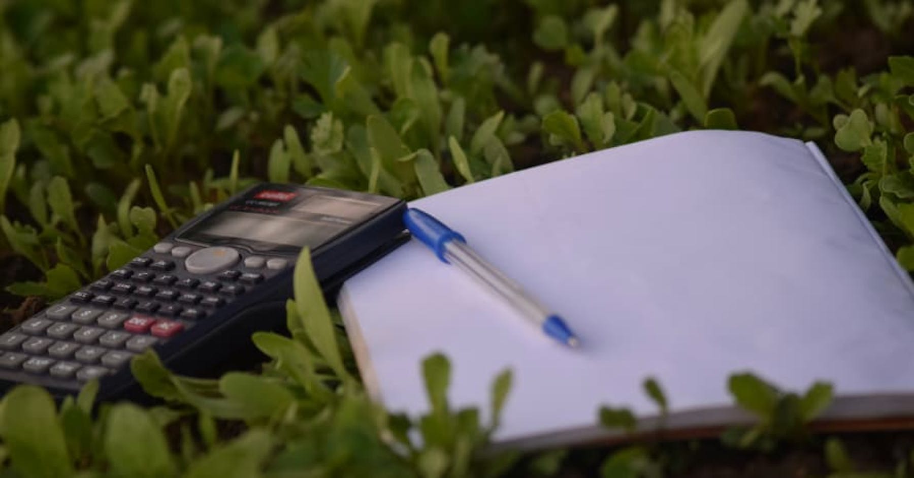 calculator and notebook with pen on grass
