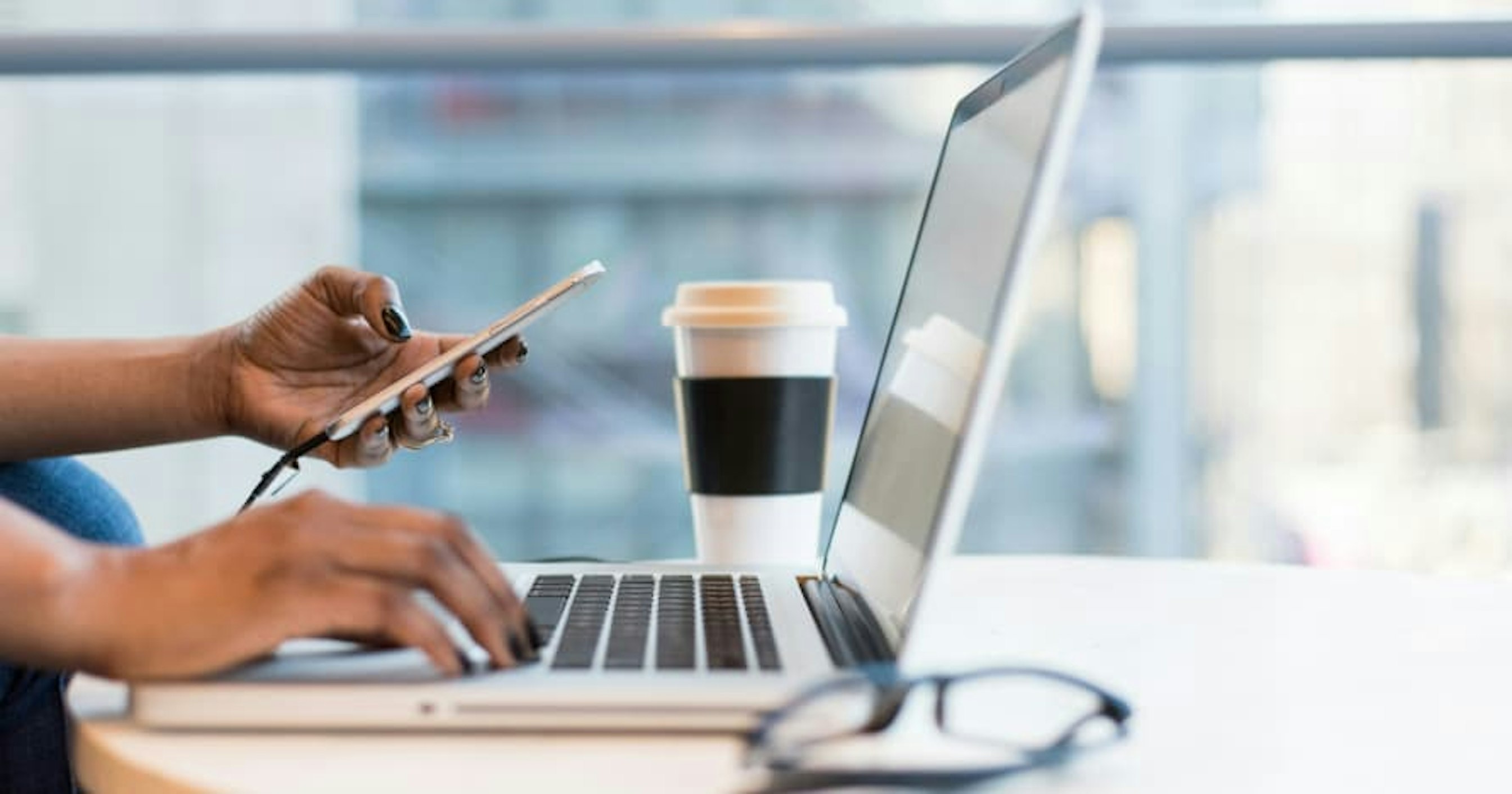 person working remotely with laptop, coffee, and glasses on table