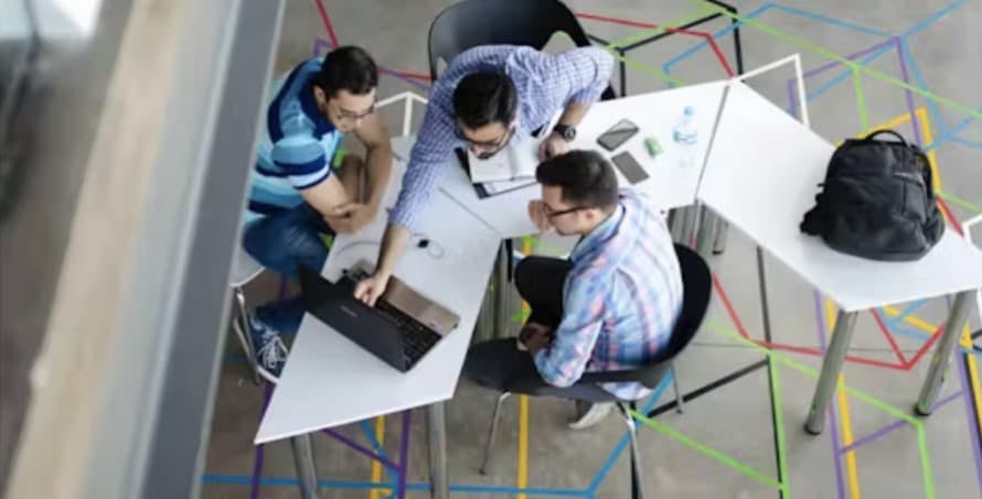 three men in a workplace looking at a laptop computer