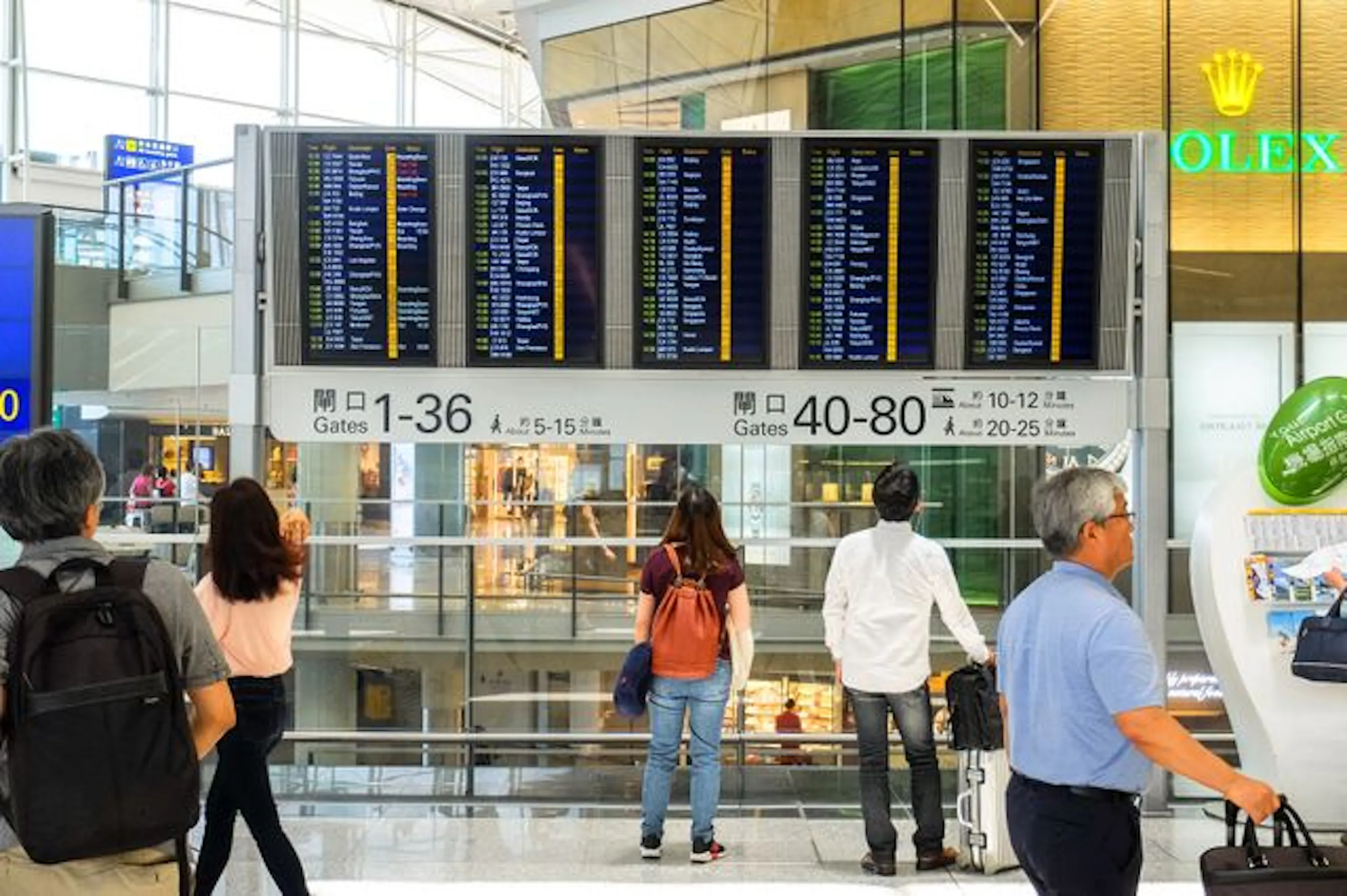 Voyageurs dans un hall de départ d'aéroport, devant les écrans d'embarquement.