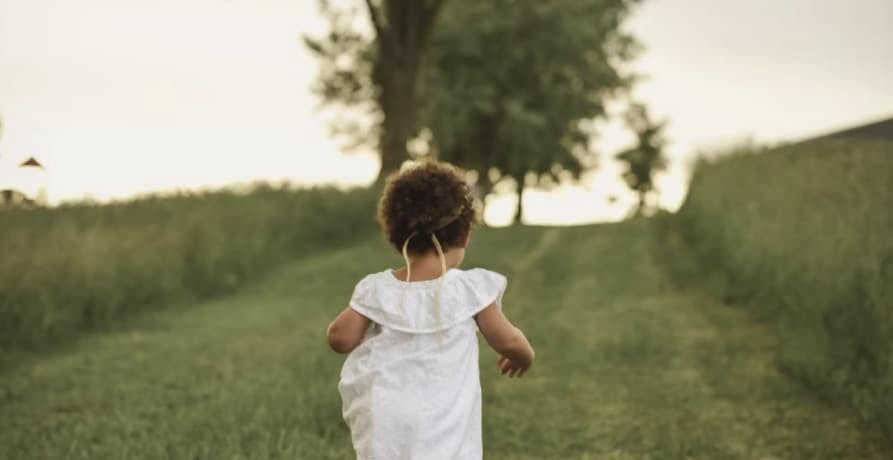 Girl standing on grass field facing trees