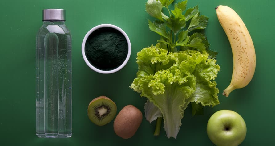leafy greens, kiwi, apple, banana, botte of water, coffee with green background