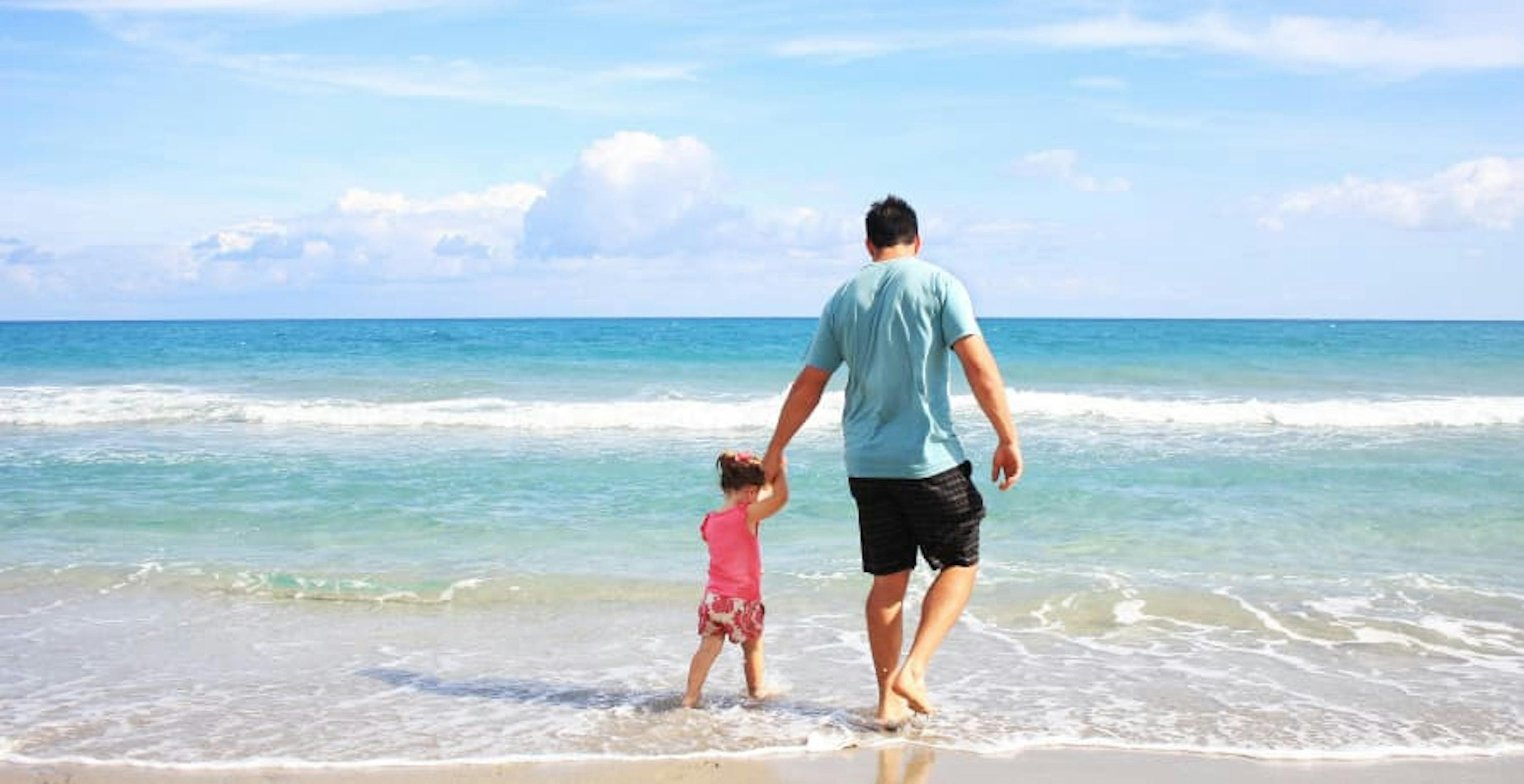 Dad holding his daughters hand as they walk in the ocean