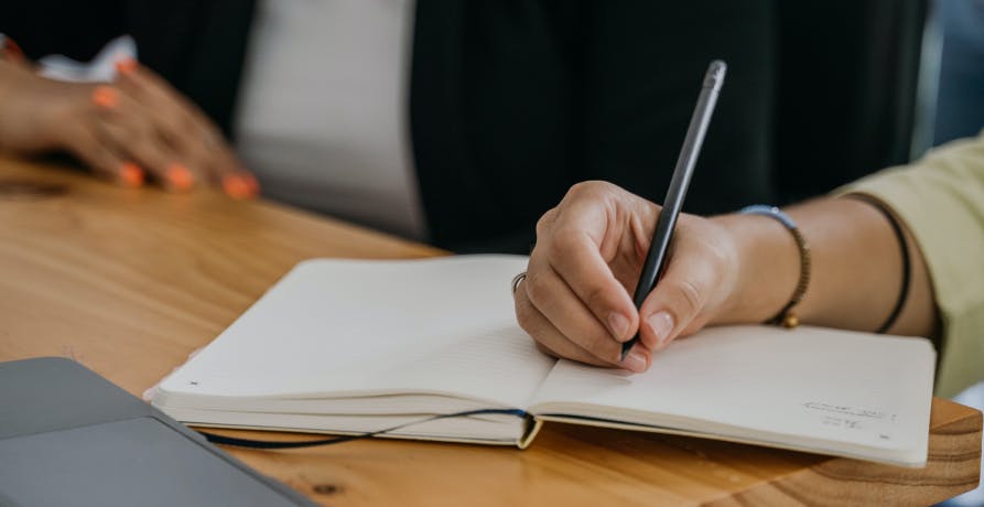 une main tenant un stylo devant un carnet