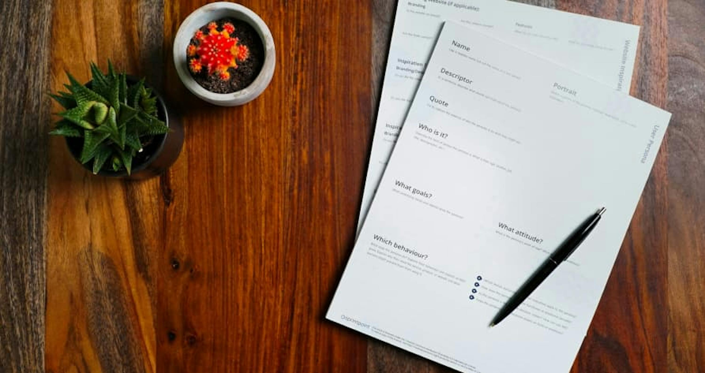 papers on desk with pen and small plants