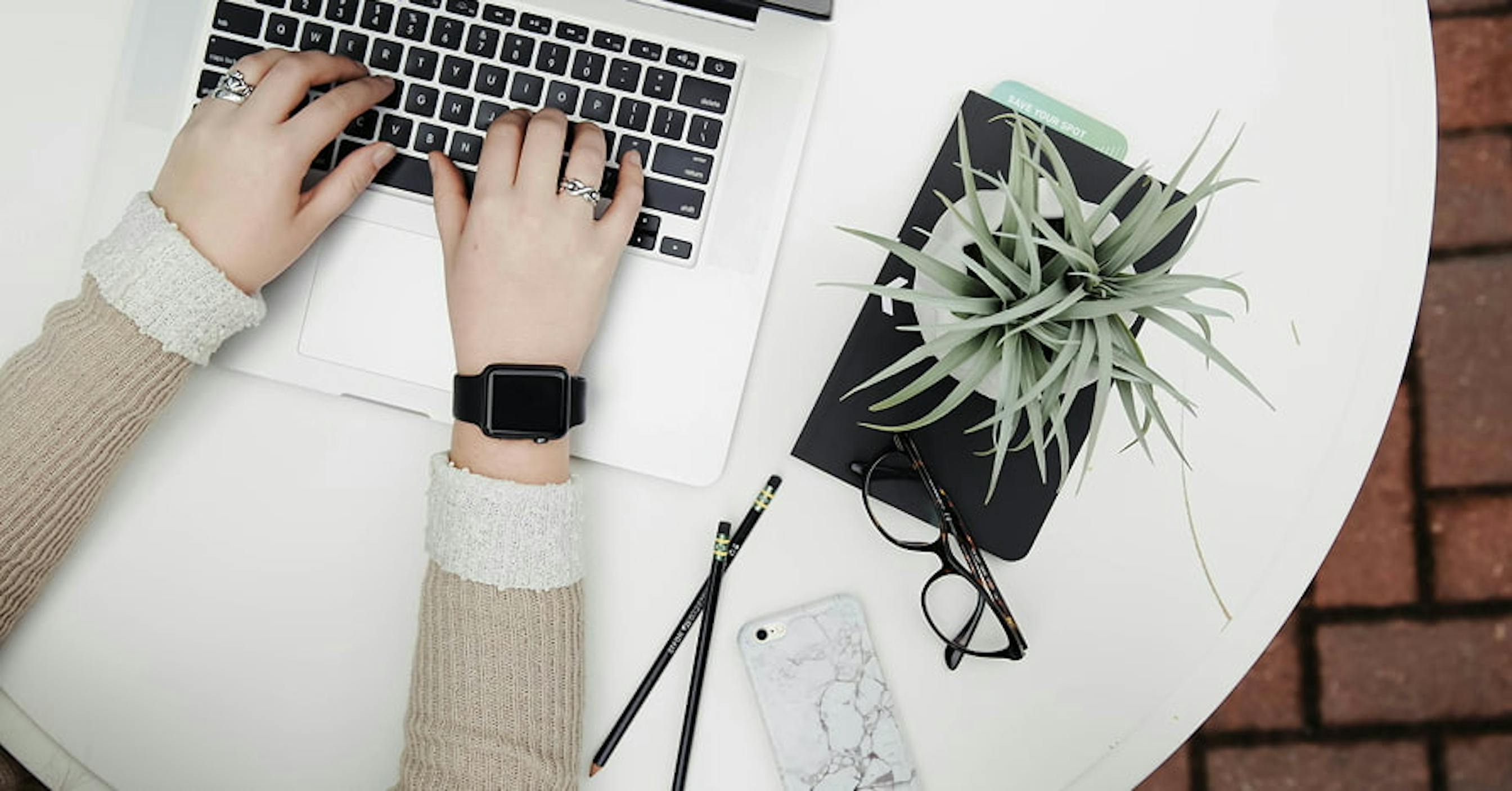 person typing on laptop with plant and glasses next to them