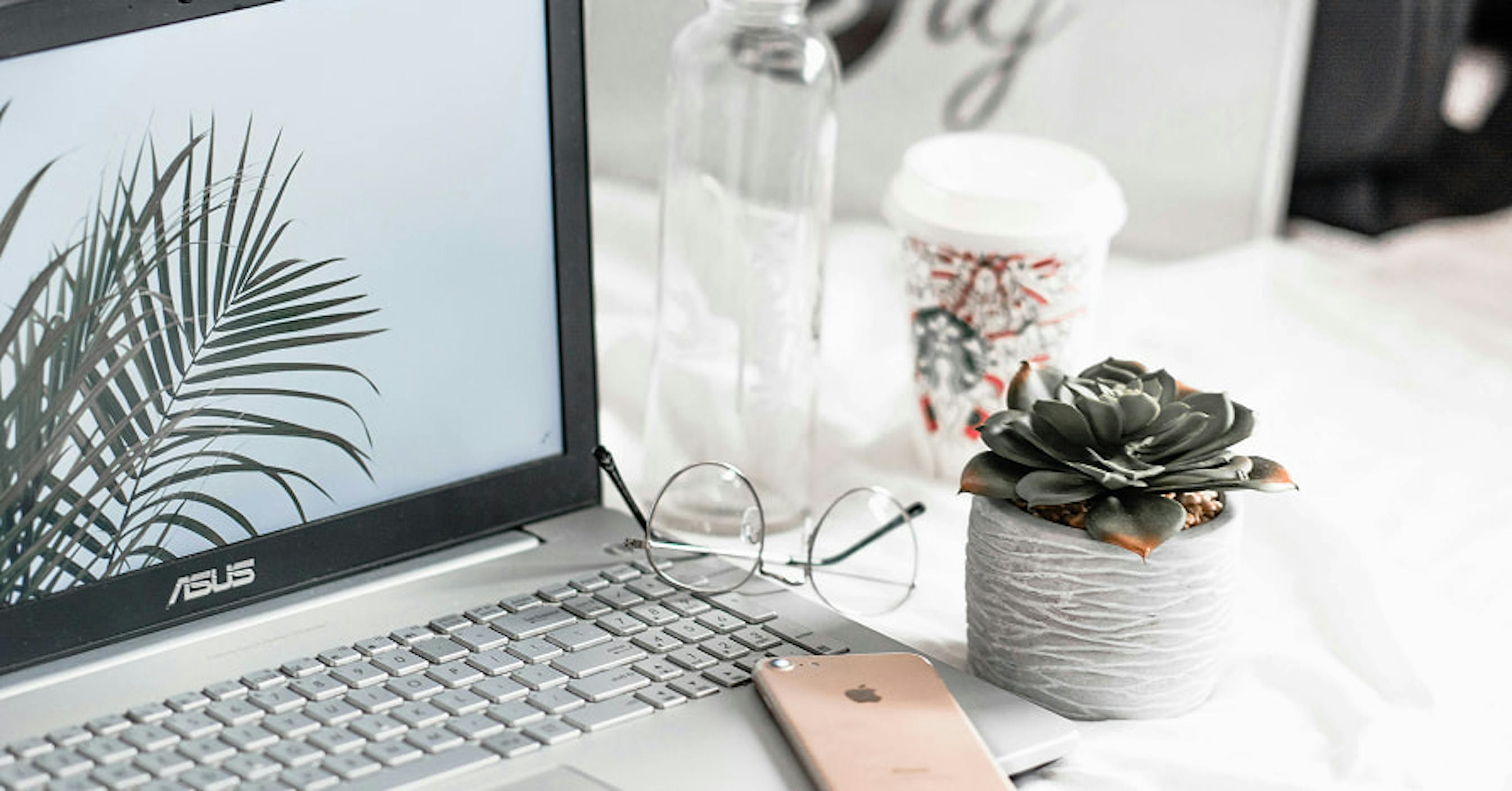 person with laptop open to plant with Christmas starbucks cup and rose gold iphone