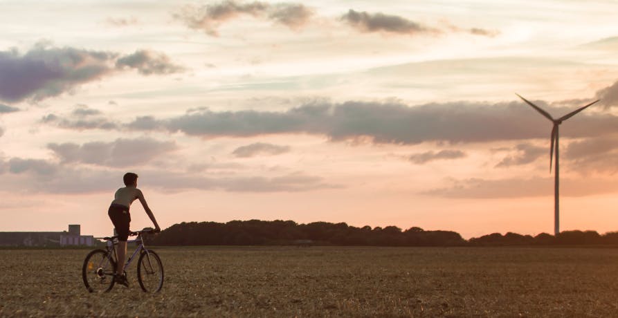 un jeune homme a vélo dans les champs devant une éolienne