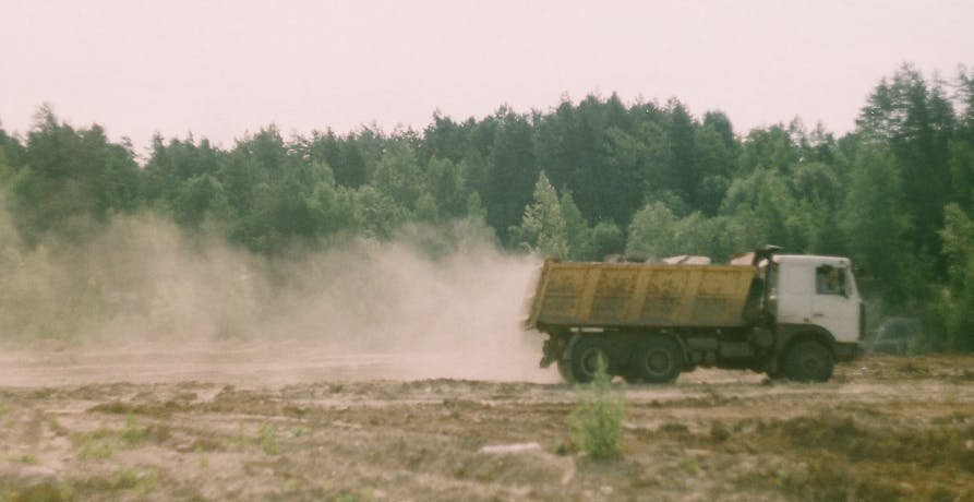 camion de chantier roulant sur de la terre et laissant un nuage de poussières derrière lui