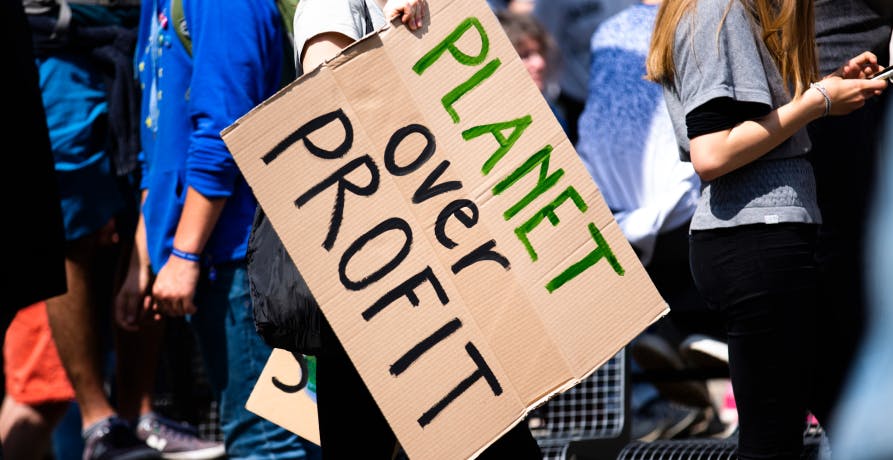 Protesters holding a sign that says planet over people