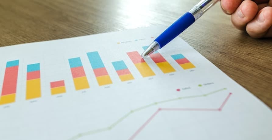 paper showing bar graphs person pointing with a blue pen