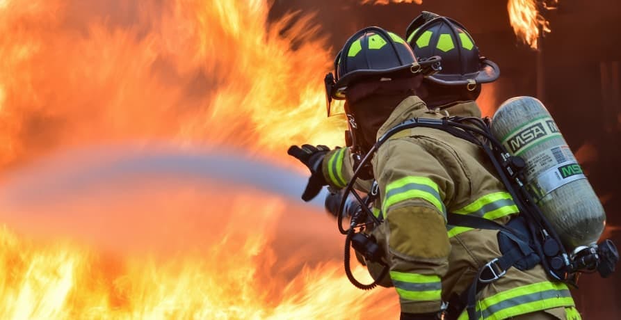 two firefighters pouring water onto large fire